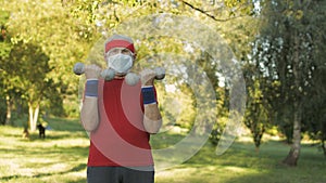 Senior man making fitness exercises with dumbbells during coronavirus virus pandemic alone in park