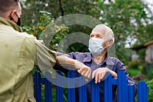 Senior man in mask having conversation with his neighbour