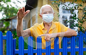 Senior man in mask waving with hand outdoors