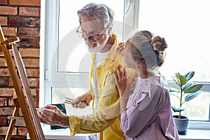 Senior man, grandfather and his granddaughter drawing, painting together