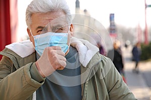 Senior man with medical mask coughing on street. Virus protection