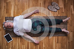 Senior man meditating on a wooden floor and lying in Shavasana pose. photo