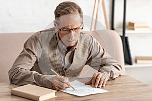 senior man with mental illness drawing on paper near book at home.