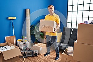 Senior man moving to a new home holding cardboard box clueless and confused expression