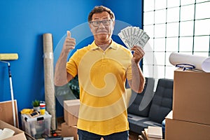 Senior man moving to a new home holding money smiling happy and positive, thumb up doing excellent and approval sign