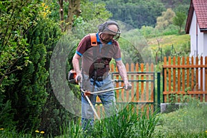 Senior man mowing grass by brush cutter in garden