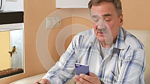 Senior man with a mustache makes a purchase from the online store credit card. He was sitting at home on the couch and