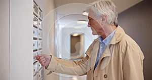 Senior man opening mailbox in lobby of apartment building and smiling receiving letter