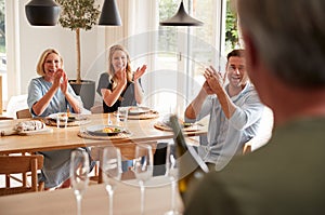 Senior Man Opens Bottle Of Champagne As Family With Adult Offspring Eat Meal Around Table At Home