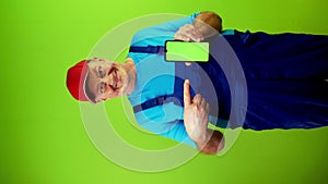 Senior man in overalls pointing with finger at green display and smiling.