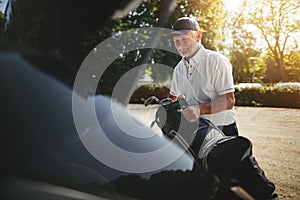 Senior man packing his golf clubs in a car trunk