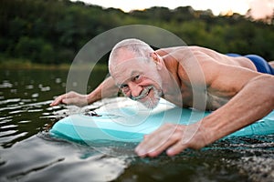 Senior man on paddleboard on lake in summer, swimming.