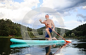 Senior man paddleboarding on lake in summer. Copy space. photo