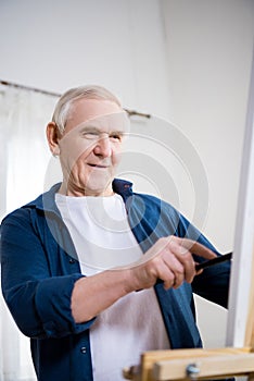 Senior man painting picture on easel at home