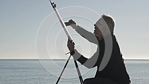 Senior man paints a picture on the beach. Elderly male artist painting the canvas on metal easel on morning calm sea