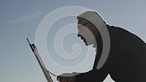 Senior man paints a picture on the beach. Elderly male artist painting the canvas on metal easel on morning calm sky