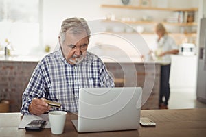 Senior man paying bills online on laptop in kitchen