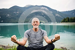A senior man pensioner sitting by lake in nature, doing yoga exercise. photo