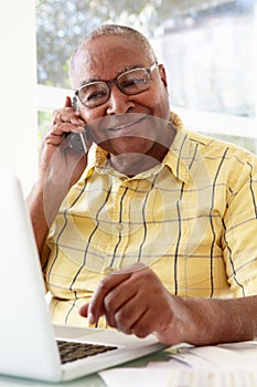 Senior Man On Phone Using Laptop At Home