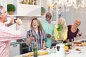 Senior man photographing laughing multiracial male and female friends cooking food at home