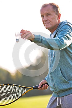 Senior man playing badminton with tennis racket in park