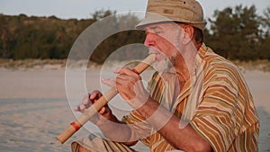 Senior man playing bamboo flute on the beach at sunset