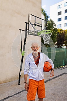 Senior man playing basketball outdoors on basketball court in city. Older, vital man has active lifestyle, doing sport