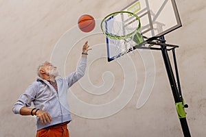 Senior man playing basketball outdoors on basketball court in city. Older, vital man has active lifestyle, doing sport