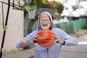 Senior man playing basketball outdoors on basketball court in city. Older, vital man has active lifestyle, doing sport photo