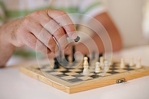 Senior man playing chess, close-up of hand.