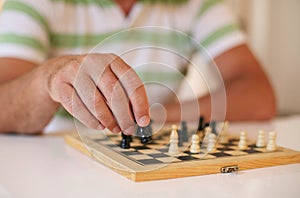 Senior man playing chess, close-up of hand.