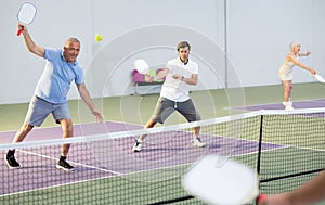 Senior man playing doubles pickleball with male partner indoors