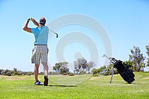 Senior, man and playing golf on field, lawn or green grass for sports, swing or taking a shot on course. Rear view of