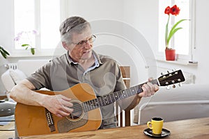 Senior man playing guitar at home in a bright living room