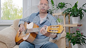 Senior man plays acoustic guitar and sings in apartment living room