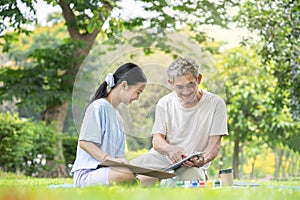 senior man point index to digital tablet to teach his granddaughter drawing