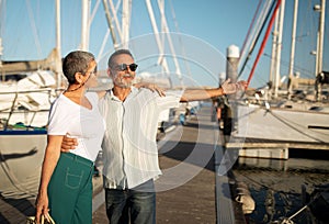 Senior man pointing at yacht at dock inviting woman outside