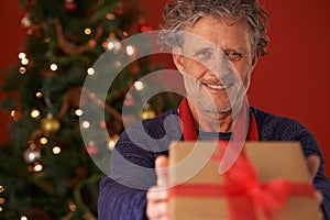 Senior man, portrait and Christmas tree with gift box for present, giving or December holiday at home. Happy male person