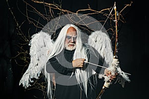 Senior man posing with angel wings. Elderly man holding two red horns. Monster with white blue eyes. Devil horror