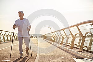 Senior man practices Nordic walking with poles on empty city footbridge