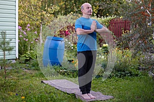 Senior man practicing yoga standing in tadasana in his garden.
