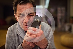 Senior man praying, holding Bible in his hands, eyes closed.