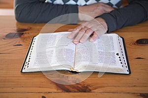 Senior man praying, reading an old Bible. Hands folded in prayer on a Holy Bible in church concept for faith, spirituality and