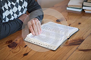 Senior man praying, reading an old Bible. Hands folded in prayer on a Holy Bible in church concept for faith, spirituality and