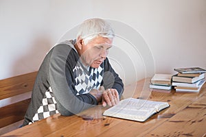 Senior man praying, reading an old Bible. Hands folded in prayer on a Holy Bible in church concept for faith, spirituality and