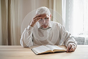 Senior man praying, reading  an old Bible in his hands