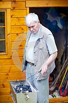 Senior man preparing fire for barbecue, outdoors