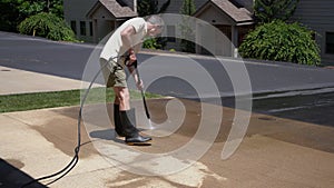 Senior man pressure spraying concrete driveway