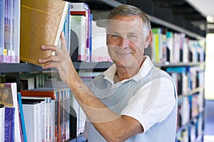 Senior man pulling a library book off shelf