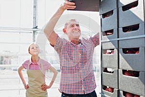 Senior man pushing forklift while talking to young female holding clipboard in greenhouse